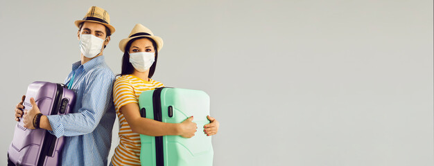 Wall Mural - Couple going on holiday trip together. Man and woman in face masks holding suitcases standing isolated on light gray text copyspace background. People ready for summer vacation, safe travel concept