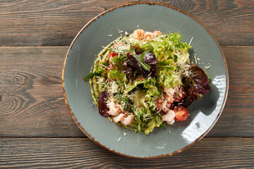 Wall Mural - From above view of healthy snack with seafood and parmesan served on avocado puree on wooden table in luxury restaurant. Tasty light salad with lettuce and shrimps on blue plate.