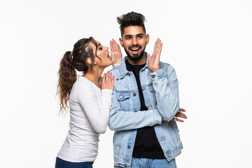 Wall Mural - Portrait of a happy young indian couple telling secrets standing together over white background