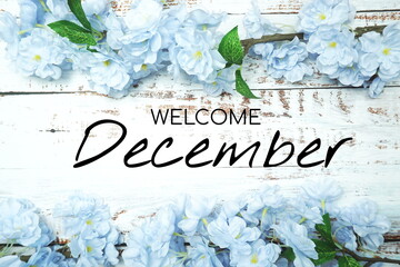 Wall Mural - Welcome December text and blue flower decoration on wooden background