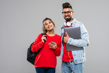 Attractive young indian couple of college students with books, laptop and school bags in a white background