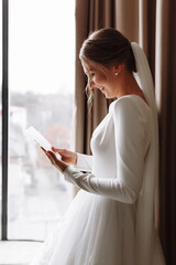 Wall Mural - Wedding day. Fees at the hotel. the bride near the window and reads the letter to the groom. Wedding vows. Preparations. Morning of the bride. bride in white dress and veil.