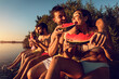 © Zoran Zeremski - Friends sitting on the edge of a pier enjoying on a summer day at the lake eating watermelon.