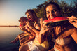 © Zoran Zeremski - Friends sitting on the edge of a pier enjoying on a summer day at the lake eating watermelon.