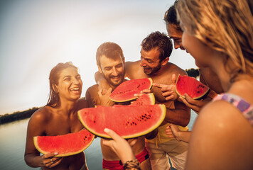 Wall Mural - Friends standing on a pier eating watermelon and enjoying a summer day at the lake.