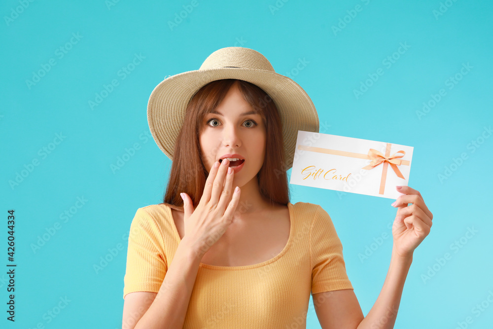 Surprised young woman with gift card on color background