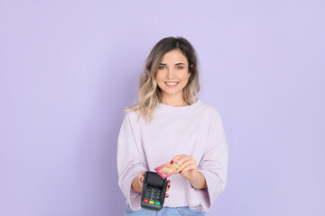 Wall Mural - Young woman with payment terminal and credit card on color background