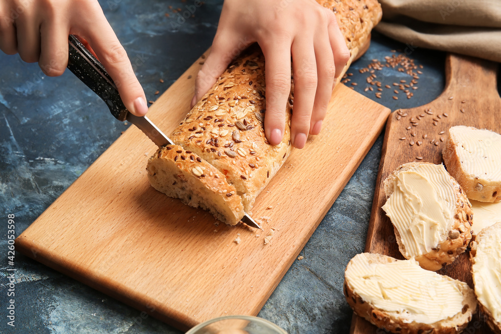 Woman cutting fresh bread on wooden board, closeup