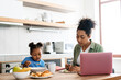 © Drobot Dean - Black woman working while having breakfast with her daughter