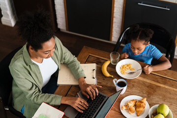 Wall Mural - Black woman working while having breakfast with her daughter