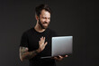 © Drobot Dean - Bearded smiling man with tattoo waving hand and using laptop