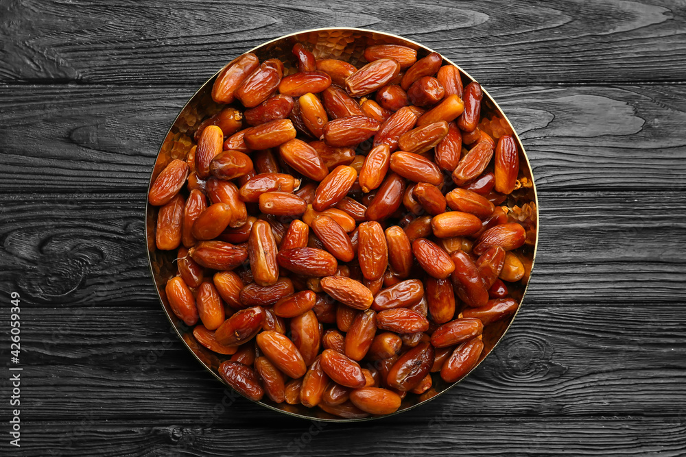 Plate with sweet dried dates on dark wooden background