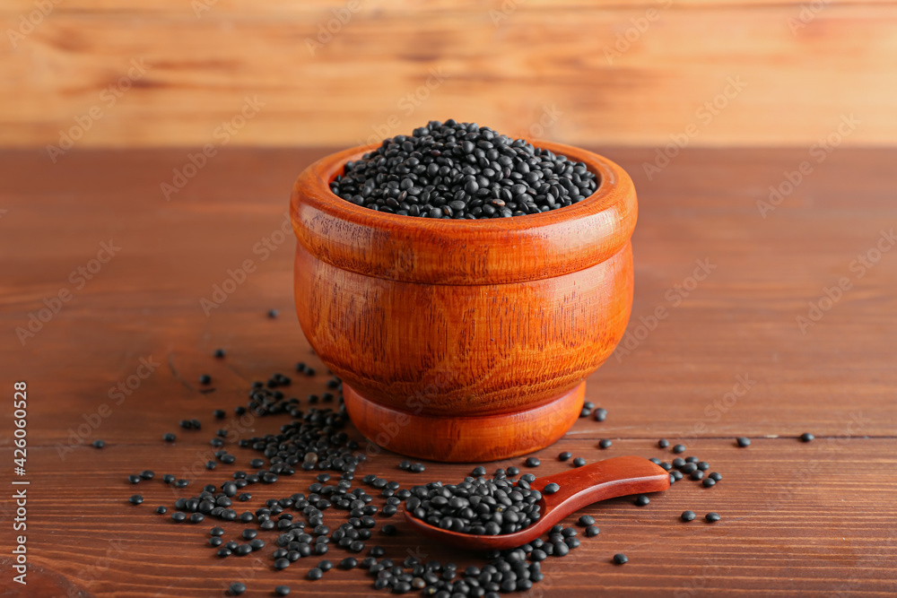 Bowl and spoon with black lentils on wooden background