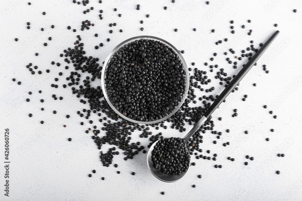 Bowl and spoon with black lentils on light background