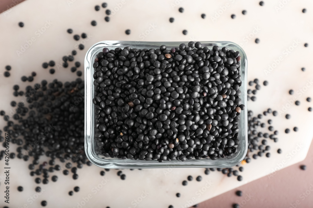 Bowl with black lentils on color background
