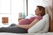 © olsima - Attractive pregnant woman is sitting in bed and holding her belly. Last months of pregnancy.