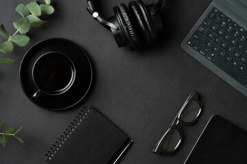 Fototapete - Top view of modern office workspace with laptop computer, cup of coffee, headphones, glasses, paper notebook, tablet on black table.