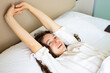 © Parten - Pretty brunette young woman waking up lying in white comfortable bed, stretching arms raising hands up after sleep well, wearing pajamas. Smiling looking in distance, planning new day. Good morning.