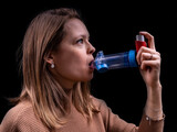 Fototapeta  - Young women taking asthma medication with an inhaler and spacer with a black background