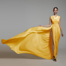 Fashion Woman In Long Silk Yellow Dress. Gray Background