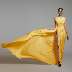 fashion woman in long silk yellow dress. gray background