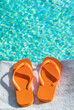 © Tetra Images - Orange flip flops on towel at poolside