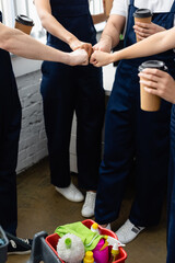 Wall Mural - Cropped view of cleaners doing fists bump while holding coffee to go near detergents in office