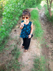 Poster - little child girl playing with flower in hands wearing sunglasses,outdoor green field,