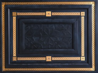 Geometric design fragment of modern luxury black wooden entrance door with carved panel and golden patina frames with classical orient pattern.