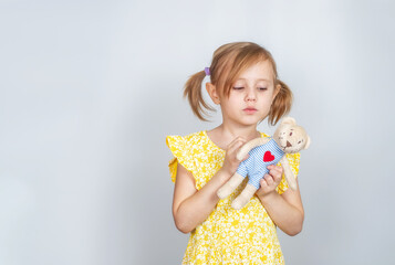 Little Caucasian girl with teddy bear looks thoughtfully at toys