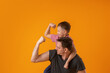friendly man and a small boy with their hands raised show their muscles and strength. Father and son pose on a yellow background in the studio.