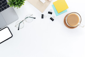 Wall Mural - Top view of a desk with a laptop, eyeglasses, notebooks, post-it, and mobile phones isolated on  white background with copy space