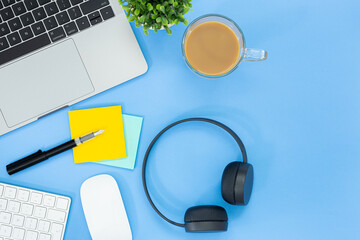 Wall Mural - Top view of a desk with a laptop, keyboard, mouse, notebooks, post-it, and headphones isolated on blue background