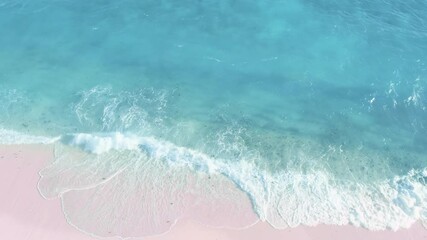 Wall Mural - Top-down aerial of ocean waves crashing, foaming on pink sand beach. Nature nobody seascape. Sandy shore of light blue water. Tropical turquoise wavy coastline. Unique tourists landmark on Bahamas