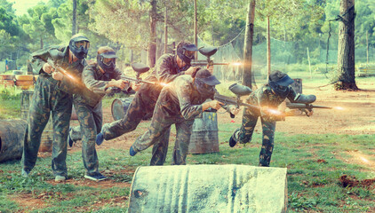 Poster - Team of happy cheerful adult people playing paintball on battlefield outdoor, running with guns