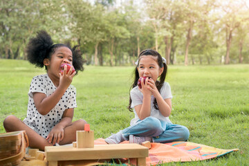 Happy cheerful ethnic girls eat apple together at outdoors park , Relationship little kids, Diverse ethnic concept.