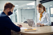 © Drazen - Businesswoman and her colleague with face masks working in the office separated with sneeze guard between them due to coronavirus pandemic.