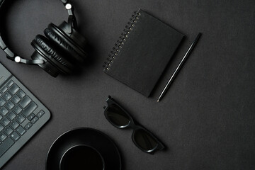 Fototapete - Luxury black workspace with headphones, laptop keyboard, glasses, cup of coffee, paper notebook and pen on leather background. Flat lay, top view.