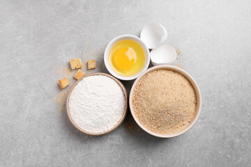 Fresh breadcrumbs, flour and egg on light grey table, flat lay