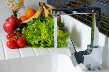 Bunch of different raw organic fruits, vegetables and greens lying in pile on a white kitchen counter near the sink. Close up, copy space for text, background, top view.