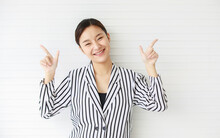 Portrait Shot Of Asian Young Confident Happy Female Businesswoman Wears Black White Stripe Casual Suit Stand In Front Wall Smiling Hold Hands Point Fingers And Look Up Above On Empty Copy Space