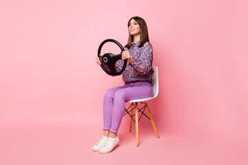 Full length photo portrait of confident woman with steering wheel sitting on white chair isolated on pastel pink colored background