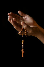 Praying Hands Of Indian Catholic Woman With Wooden Rosary Isolated On A Black Background.