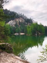 The green forest is reflected in the water. Rock on the lake shore. Summer landscape	