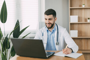 Young male doctor conducting online video consultation on laptop in his office