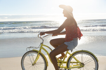 Wall Mural - Happy mixed race woman having fun on beach holiday riding on bicycle at sunset