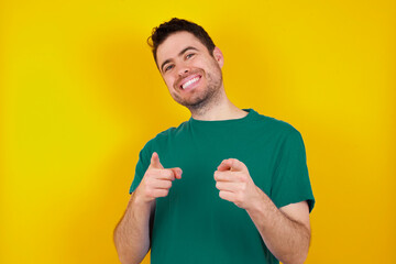 Poster - young handsome caucasian man wearing green t-shirt against yellow background pointing fingers to camera with happy and funny face. Good energy and vibes.