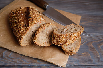 homemade bread sprinkled with flax seeds and sesame lies on a rustic plank table, next to it lies a knife, with a wooden handle