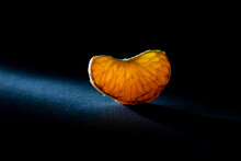 Juicy Mandarin Slice Illuminated By A Ray Of Light Macro Photography. A Piece Of Bright Orange Tangerine Close-up On A Black Background. A Slice Of Mandarine Fruit In The Backlight Closeup Photo.