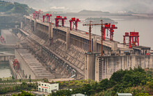 Three Gorges Dam, China - May 6, 2010: Yangtze River. Down River Side Of Dam With Hydroelectric Plant. Red Flood Control Door Lifts On Top Under Foggy Morning Sky. Plenty Of Electric Cables.